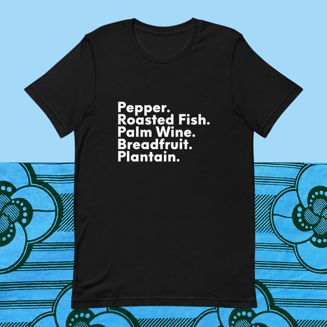 One black shirt with white text that reads "Pepper. Roasted Fish. Palm. Wine. Breadfruit. Plantain." on a blue background.